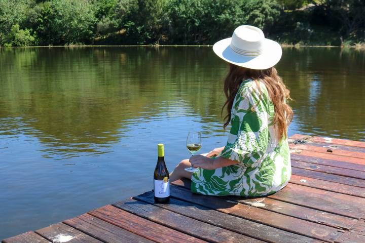 A guest in a sun hat with a glass of wine on the jetty at the dam